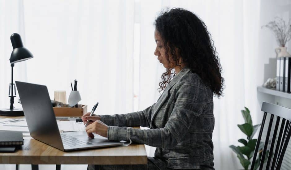 une femme à un bureau devant un ordinateur, en train d'écrire sur un carnet