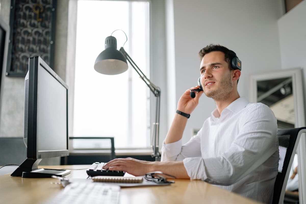 un homme du service client avec un casque, à son bureau devant un écran, lampe en arrière-plan