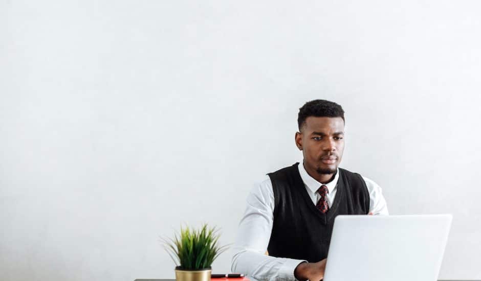 un homme devant un bureau avec un ordinateur portable et une plante verte, fond blanc
