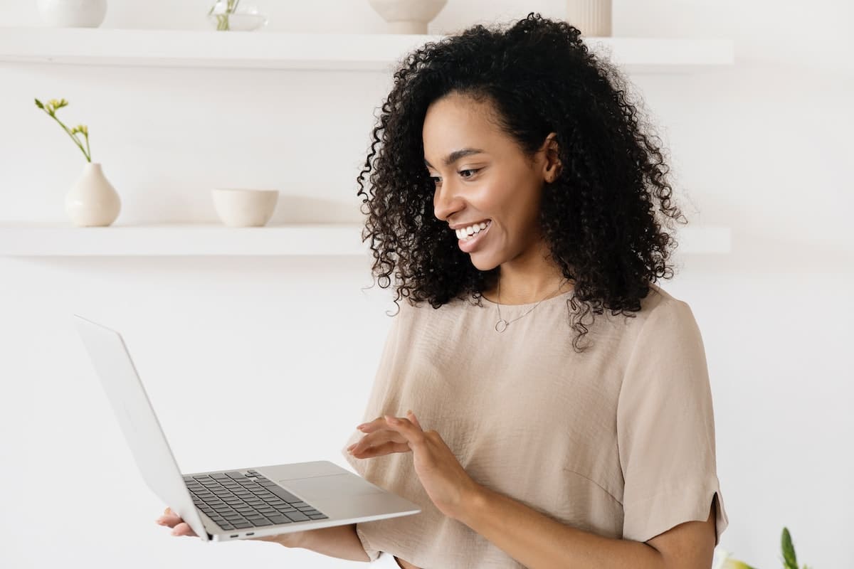une femme souriante tenant un ordinateur portable gris dans ses mains