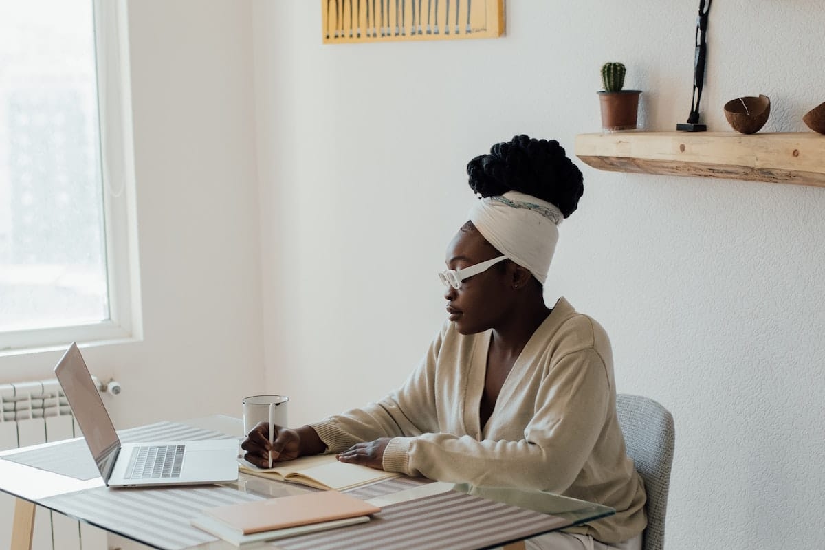 une femme à son bureau en train d'écrire sur un papier, ordinateur devant elle