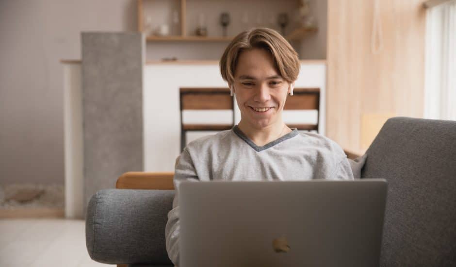 un homme sur un canapé avec des écouteurs, souriant devant un ordinateur portable