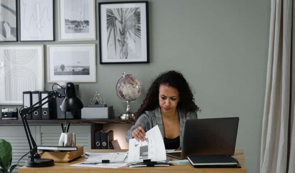 une femme à son bureau avec des documents et un ordinateur. Cadres au mur derrière elle