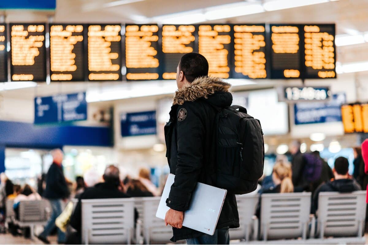 un voyageur de dos avec un ordinateur portable dans les mains dans un aéroport, panneaux d'affichage en arrière-plan