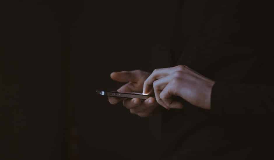 Une personne tenant un smartphone dans le noir, on ne voit que ses deux mains et l'écran allumé