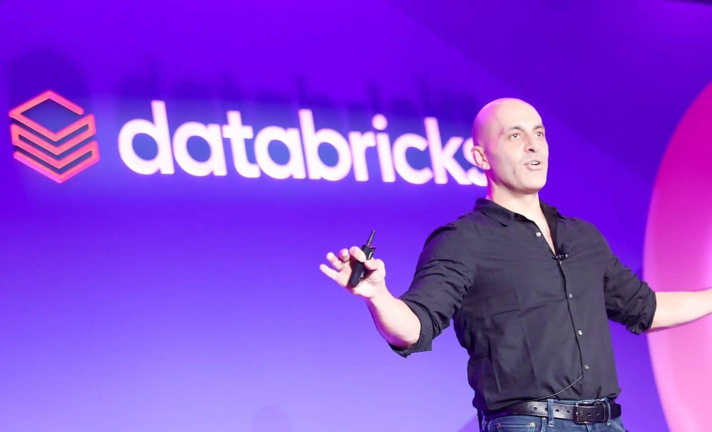 Photographie de Ali Ghodsi, PDG et cofondateur de Databricks, sur scène avec le logo de l'entreprise dans le fond.