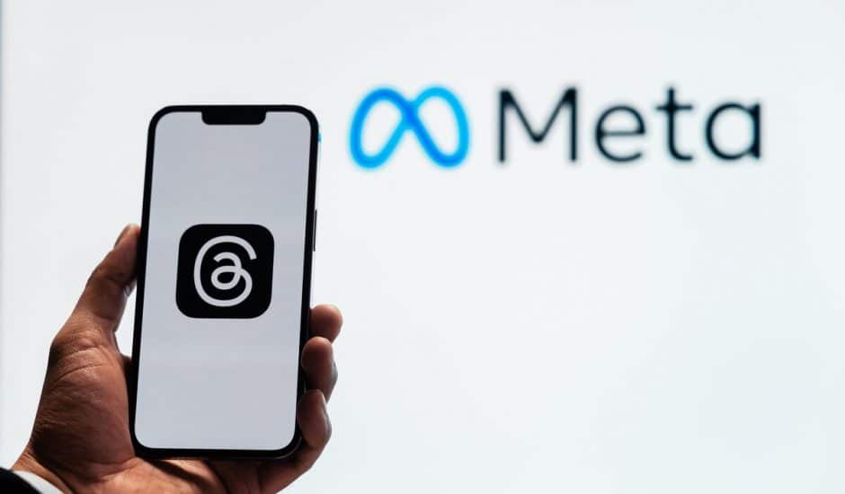 Le logo de Threads sur un téléphone avec celui de Meta en arrière plan.