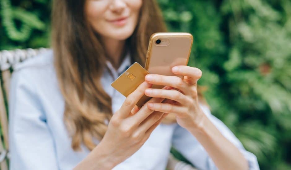 une femme tenant un smartphone et une carte bancaire