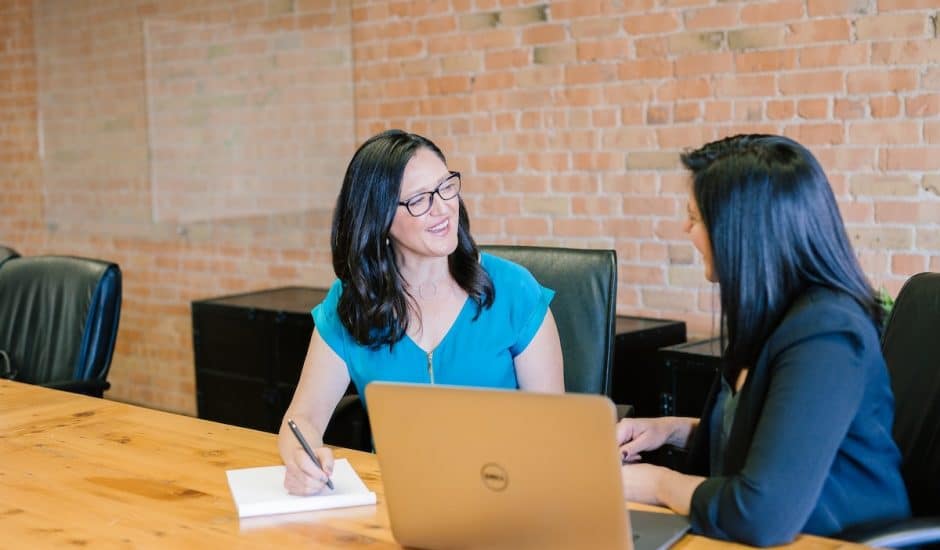 deux femmes en train de discuter dans une salle de réunion, un ordinateur et un carnet sur la table