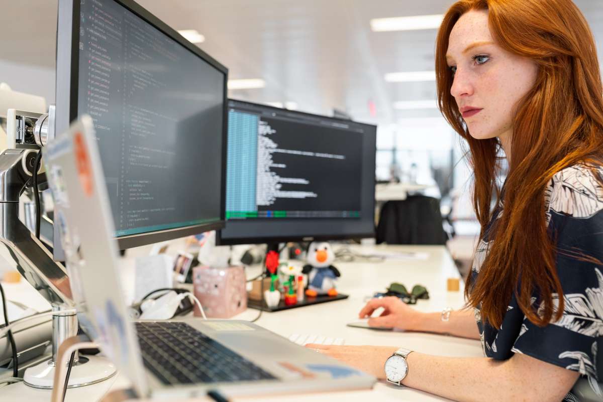 Une femme travaillant et codant devant son ordinateur de bureau.