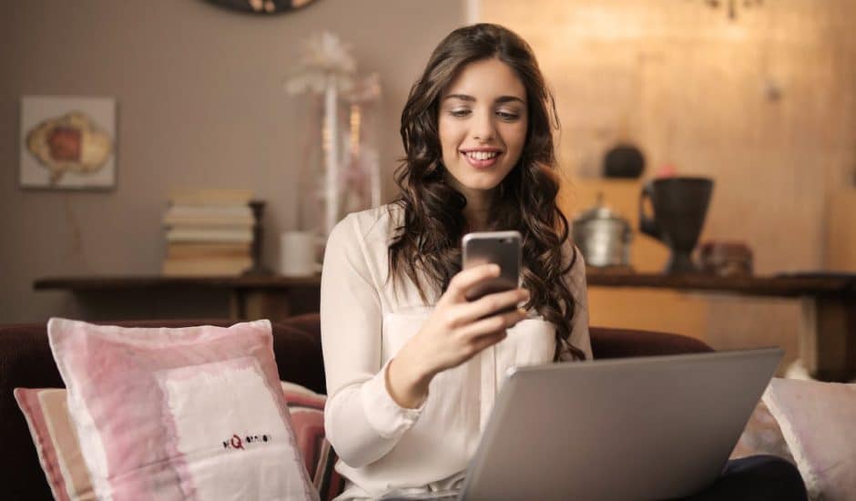 Une femme souriante sur son smartphone et devant son ordinateur