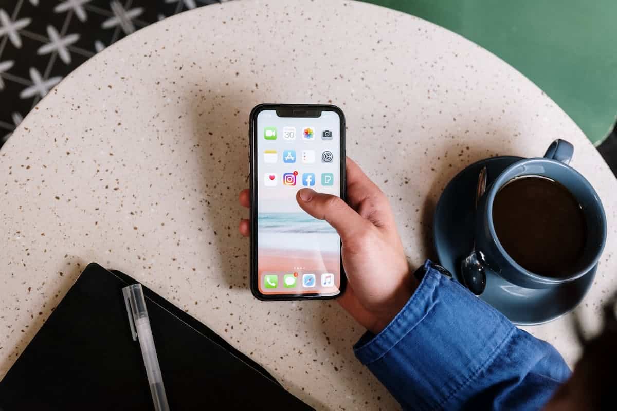 une personne tenant un iphone devant une table, une tasse à café sur celle-ci