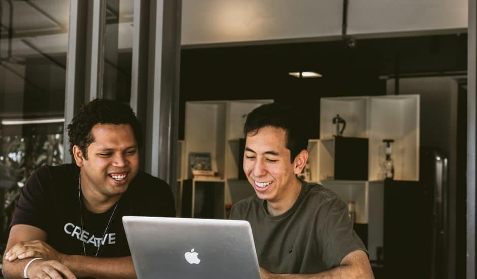 deux hommes souriant devant un ordinateur