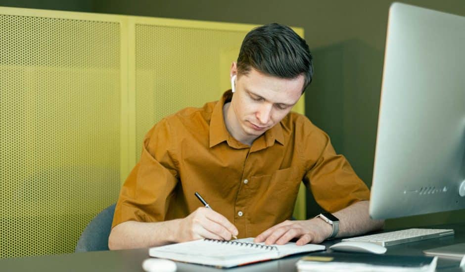 un homme en train de regarder un webinar et d'écrire sur un carnet